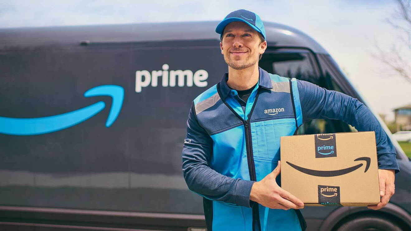 Entregador com uma caixa da Amazon. Vemos uma van com o logotipo do Prime ao fundo