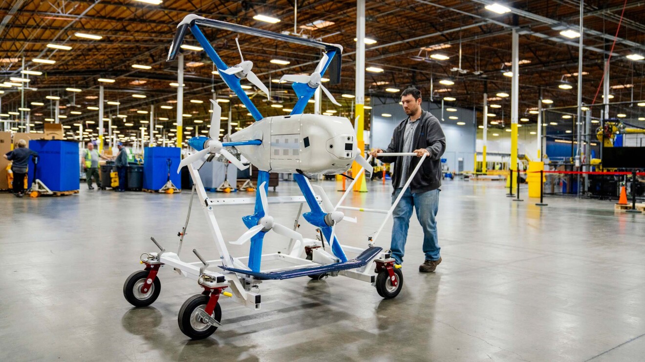 Enun centro logístico, un trabajador de Amazon trasladando un dron de entregas. 