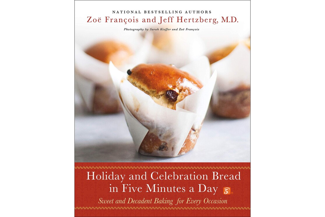 A holiday cook book with a celebration bread in parchment paper wrap, in front of other bakery treats.
