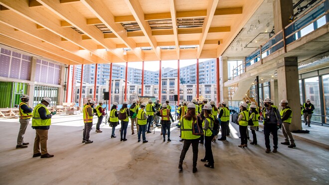 An image of people touring the construction site of Amazon's second headquarters while wearing hard hats that say