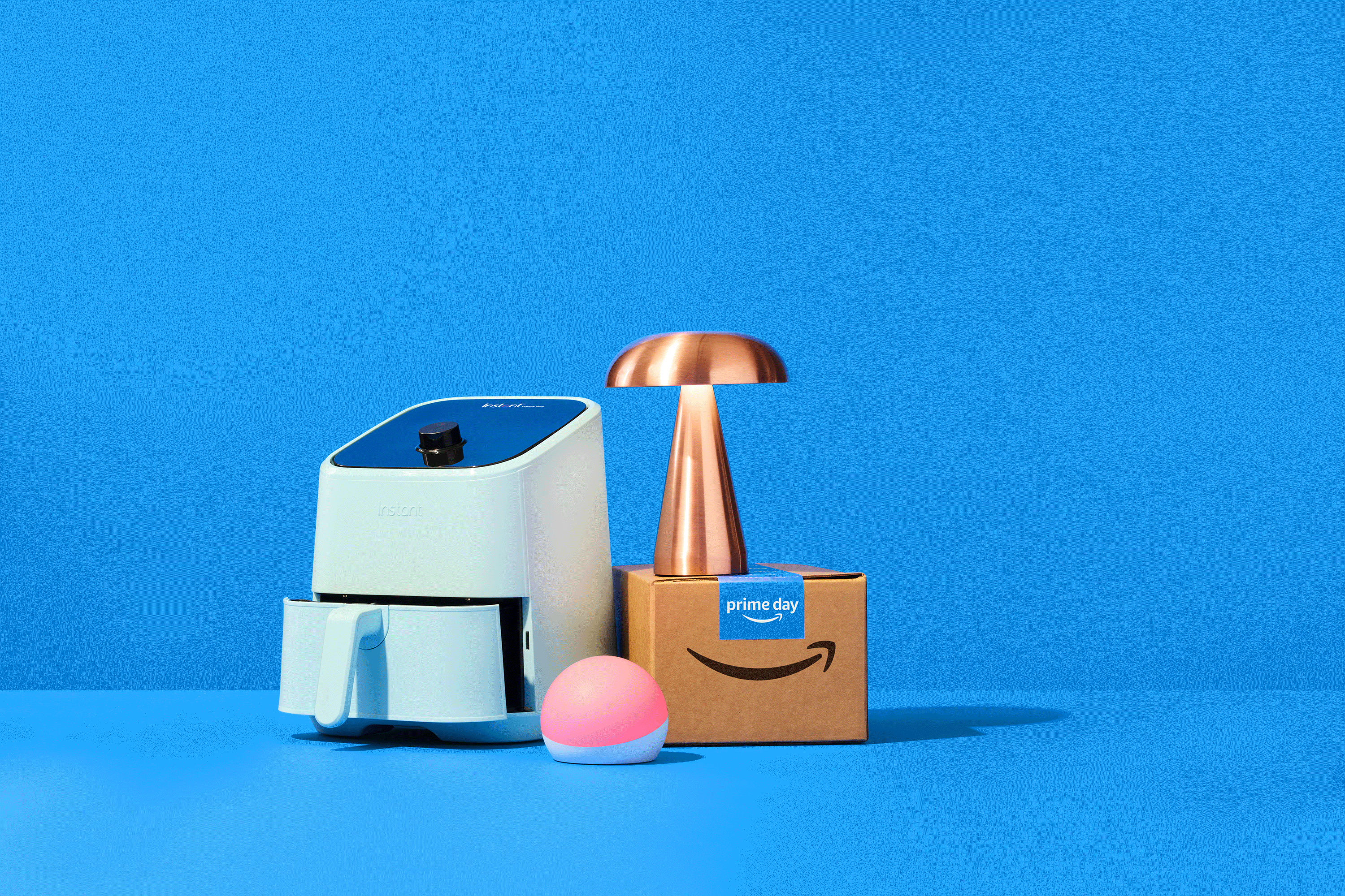 Eine animierte Illustration mit einer Air Fryer, einem Amazon Päckchen und Echo Spot auf blauen Hintergrund für den Prime Day 2024.
