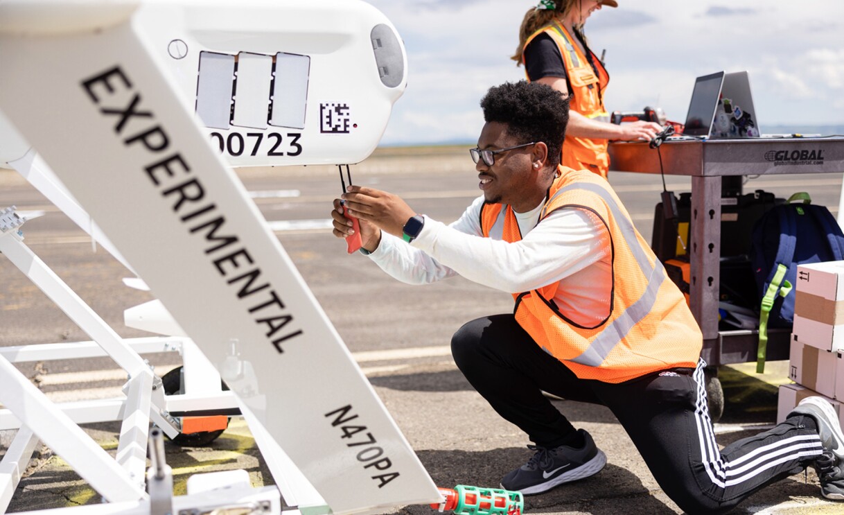 Images of Amazon employees wearing orange safety vests work on drones.