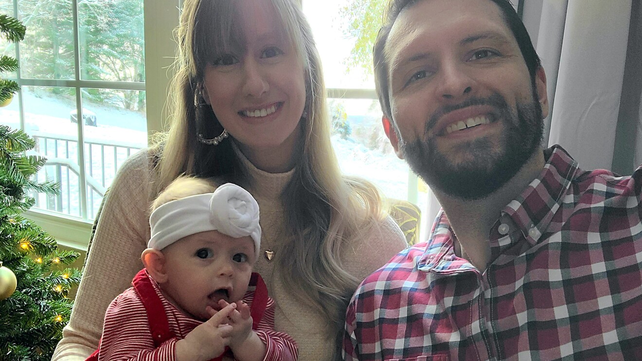 A woman and her husband pose and smile with their infant daughter