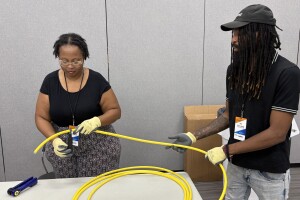 Two workers in protective gloves handling yellow cable or tubing