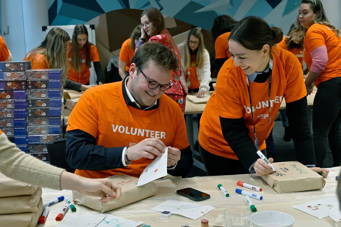 Mitarbeiterinnen und Mitarbeiter vom Amazon Standort München verpacken und dekorieren gespendete Geschenke.