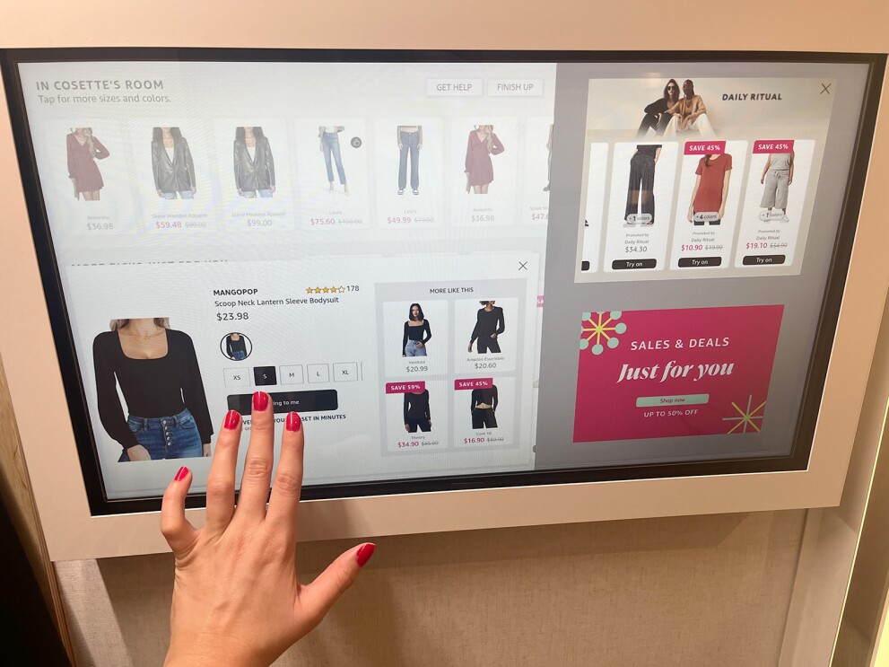 A hand selects an option on a touch screen to send more items to the fitting room.