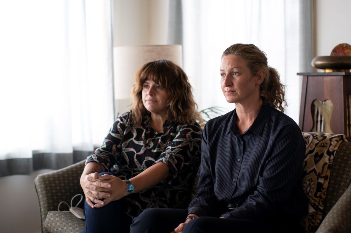 Two women are sitting in the living room watching something in front of them. 