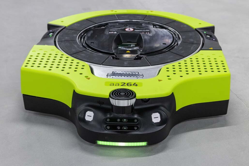 An image of a bright green, flat robot that drives around Amazon's fulfillment centers. It's face features black coloring with two small white screens on either side and a green light illuminating below.