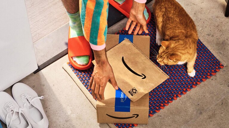 Person opening Amazon packages with orange sandals and colorful socks, cat nearby