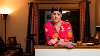 一个女人站在她公寓的厨房柜台前,温柔地微笑着拍照。她戴着黑色的发带,穿着粉红色的碎花长袍。