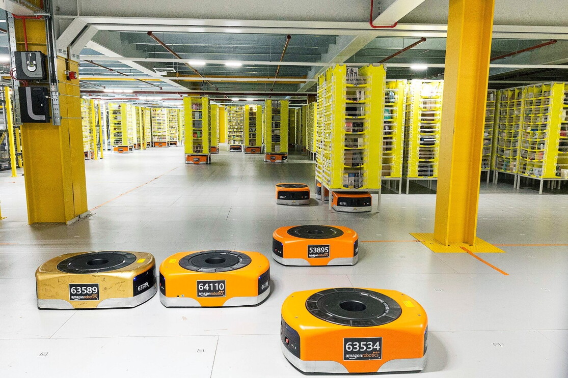 Several orange robots are pictured in a Fulfillment Center as they help move products across the floor.