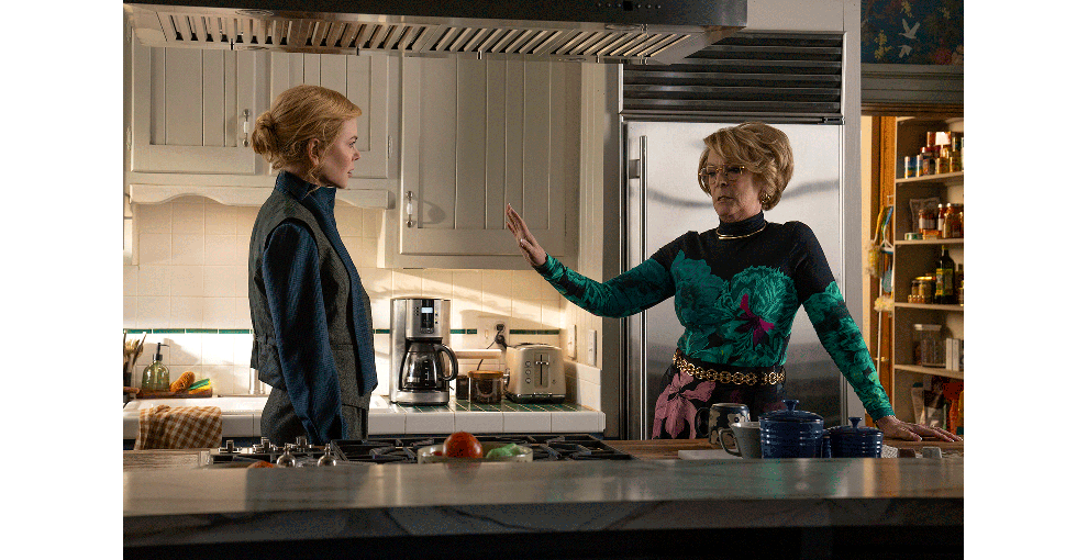 白い棚、白いタイルのキッチンで、若い女性と年配の女性が向かい合って立っている。年配の女性は、若い女性にの手の平を向けて制するようなポーズ。