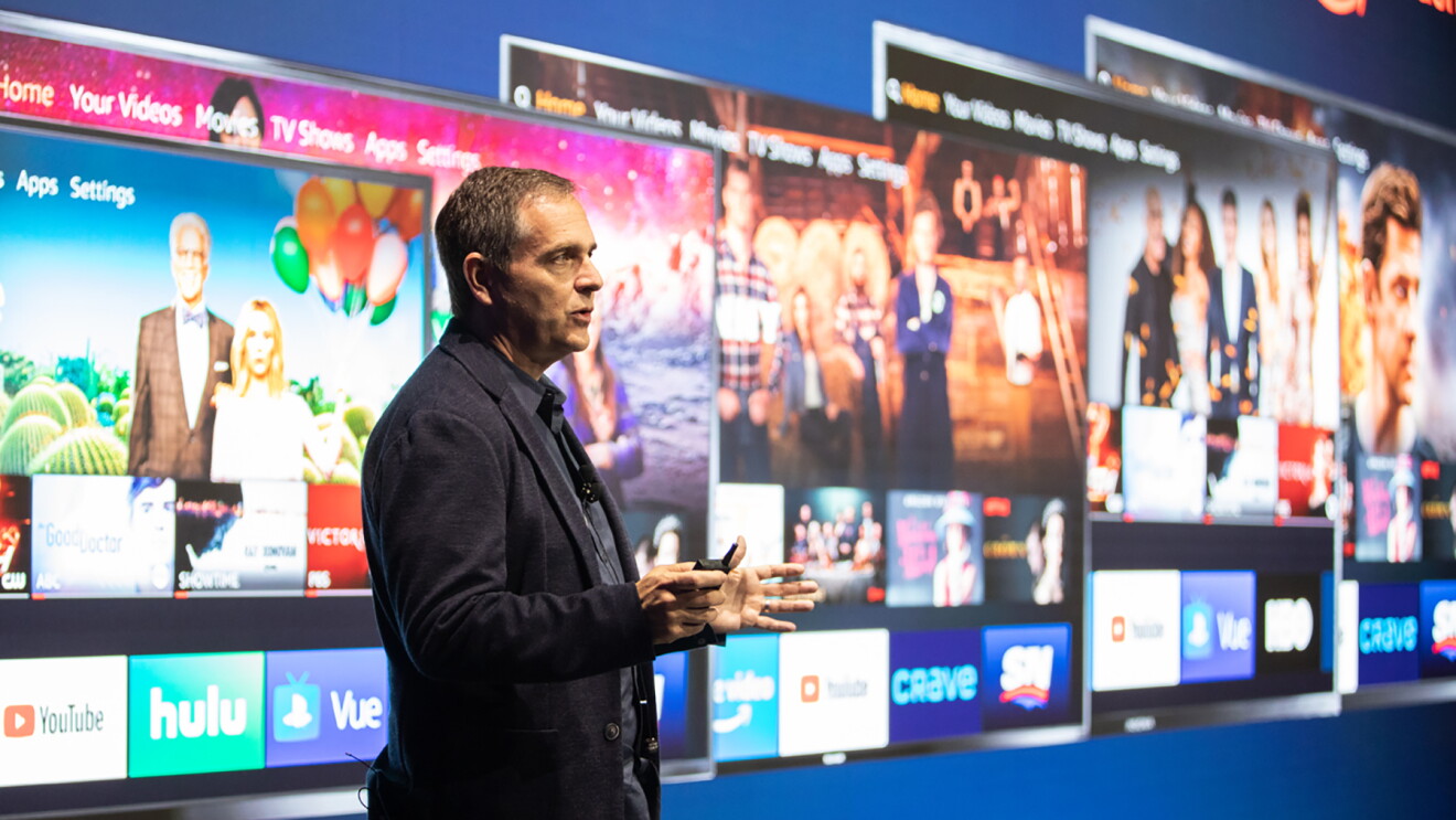 A man stands in front of a screen displaying Fire TV edition displays.