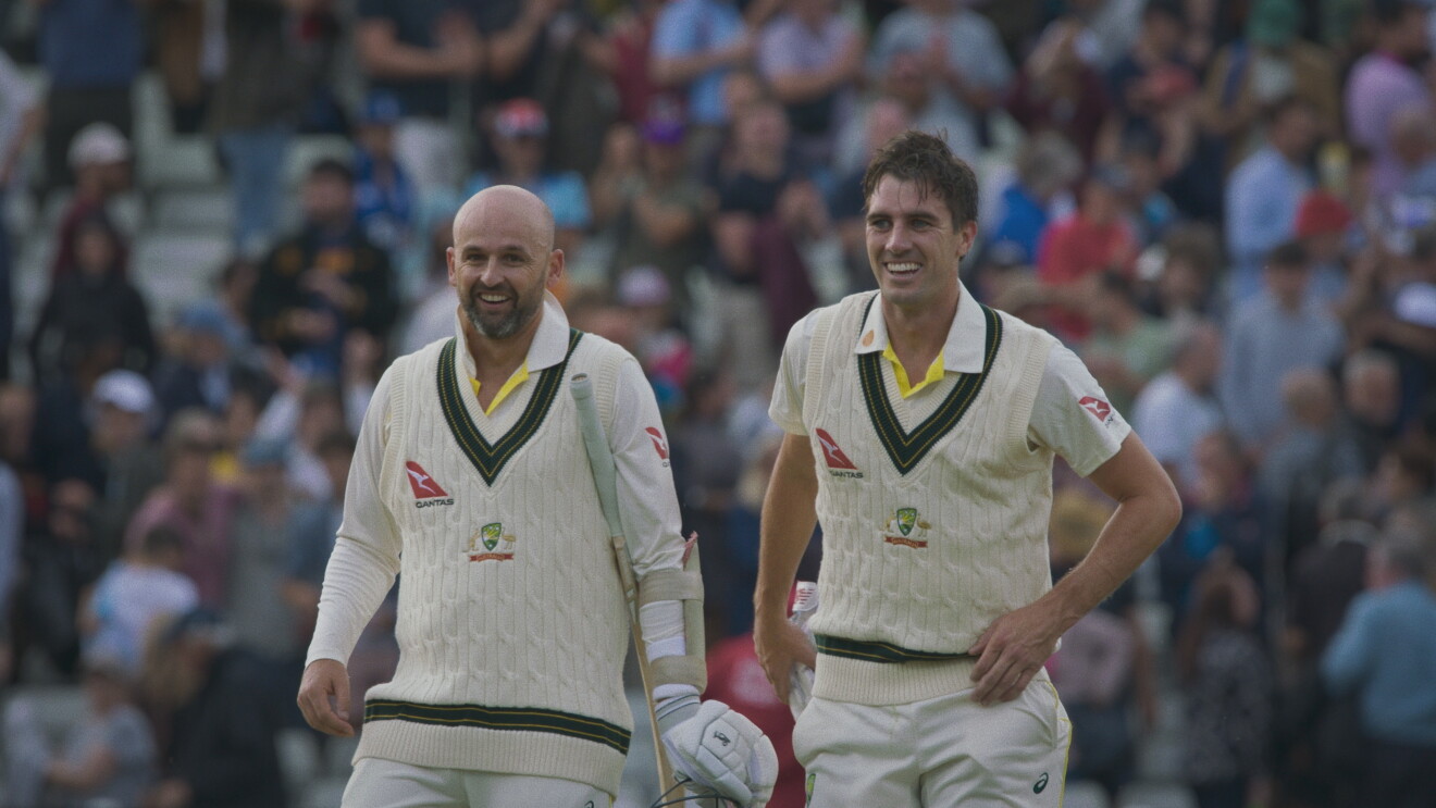 Two men in cricket gear smiling on the field 
