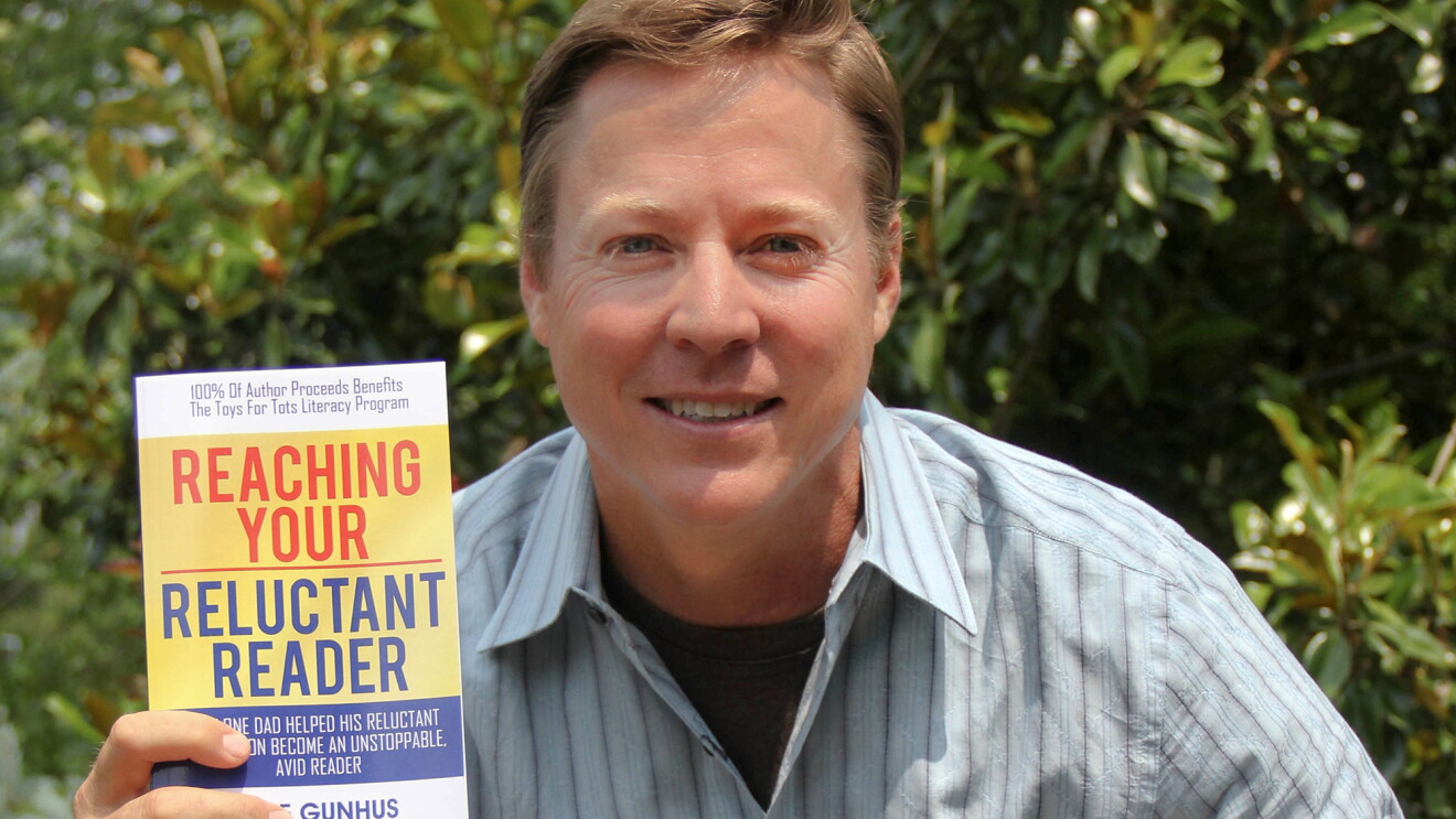 Amazon author Jeff Gunhus in a blue shirt holding up a book with the title Reaching Your Reluctant Reader.