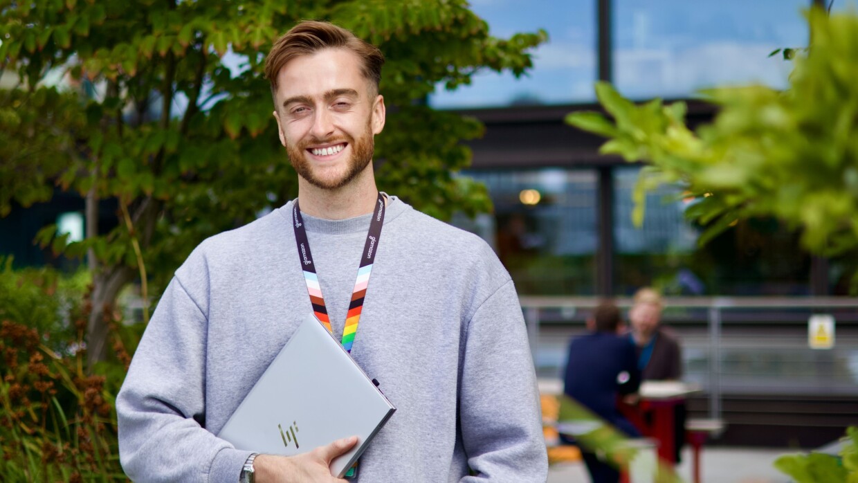 Smiling person holding HP laptop outdoors with rainbow lanyard
