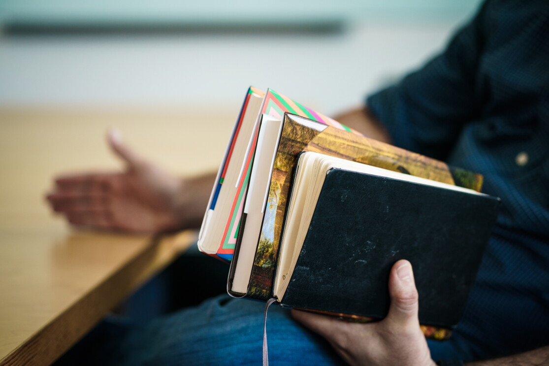Seated man holding two hardcover books and a notebook in his left hand. 