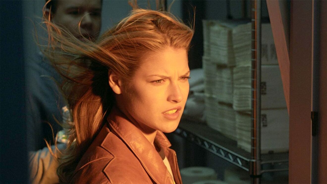 Woman with windswept blonde hair in brown leather jacket at sunset