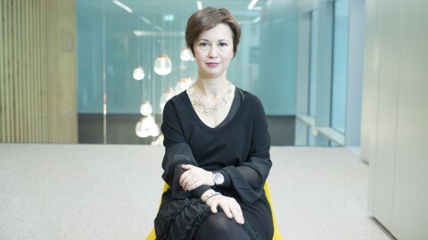 Mariangela Marseglia, directora General de Amazon España e Italia. En un espacio con una silla de color amarillo y un armario color blanco, aparece sentada en esa silla Mariangela Marseglia. Con el pelo corto de color castaño, tiene los brazos cruzados, e una muñeca tiene un reloj y en la otra una pulsera. Va con un vestido negro por la rodilla y encima un jersey negro de manga corta y de punto. Tiene un collar de piezas ovaladas unidas. De fondo se ve un cristal y una lámpara colgando del techo y que parece que da a un hall amplio. Si bien una de las paredes es un armario, la otra son unos tableros verticales de madera. 