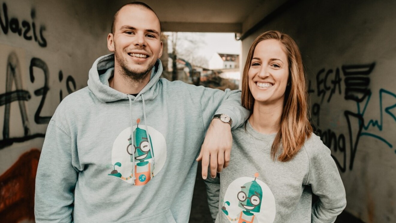 Das Team von KlimaKarl (ein junger Mann und eine junge Frau) steht in einer Unterführung und blickt lachend in die Kamera.