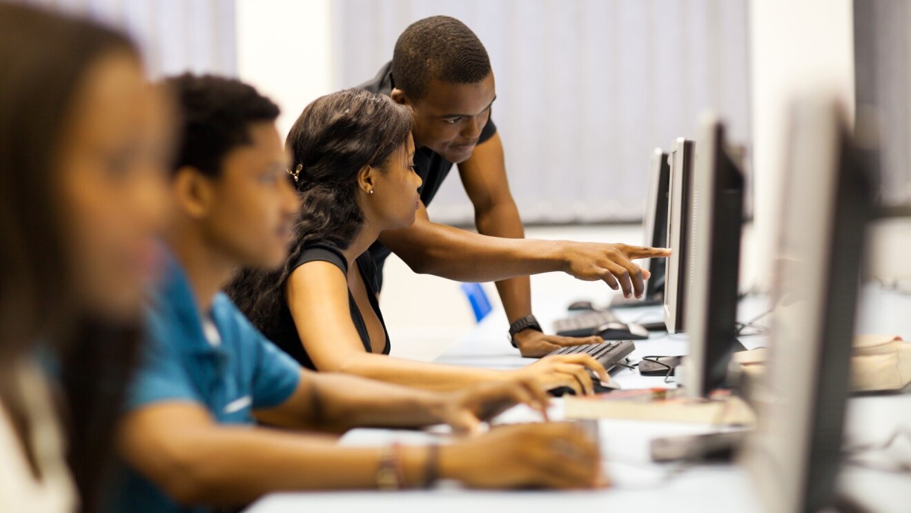 A photo of four students working in a computer lab, sitting in front of desktop computers.