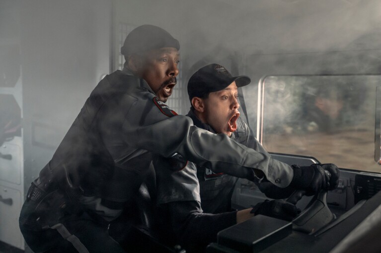 Two men looking panicked at the wheel of a vehicle filling with smoke