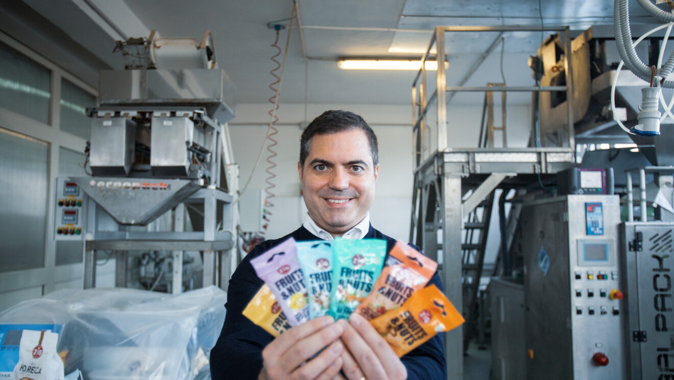 Tommaso Iozzino all'interno dello stabilimento di produzione della frutta secca. Tiene in mano alcune confezioni colorate di frutta secca mista e sorride