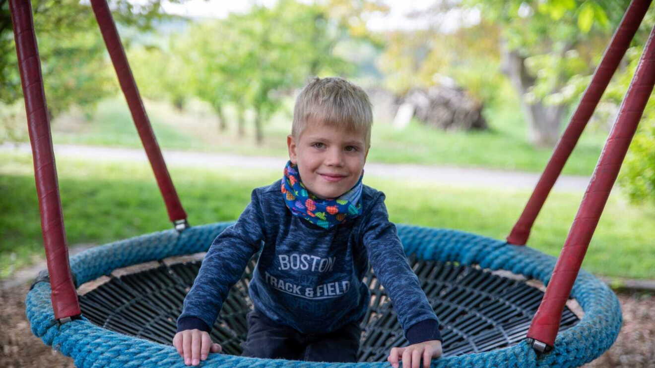 Jakob ist ein kleiner blonder Junger. Er schaukelt auf einem Spielplatz