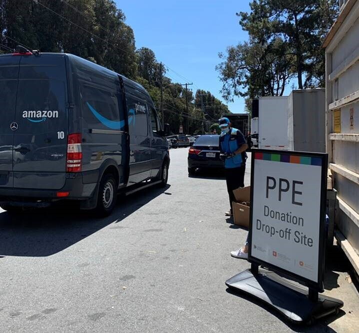 An Amazon delivery driver and van next to a sign that says "PPE Donation Drop-off Site."