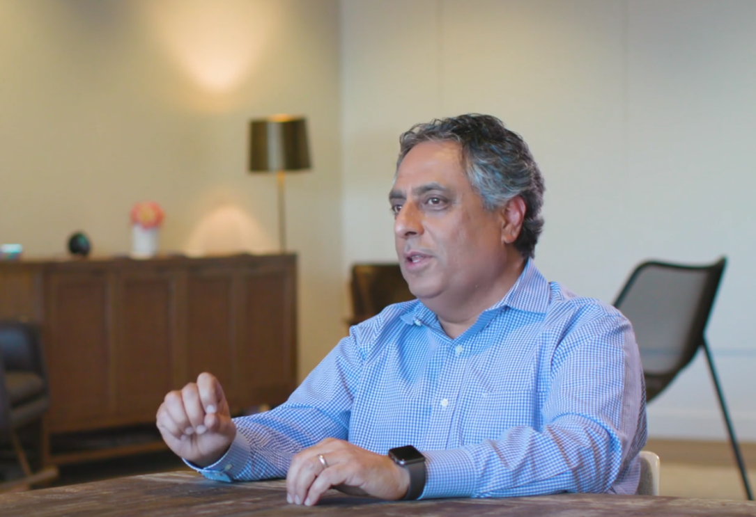An image of a man sitting at a table speaking.