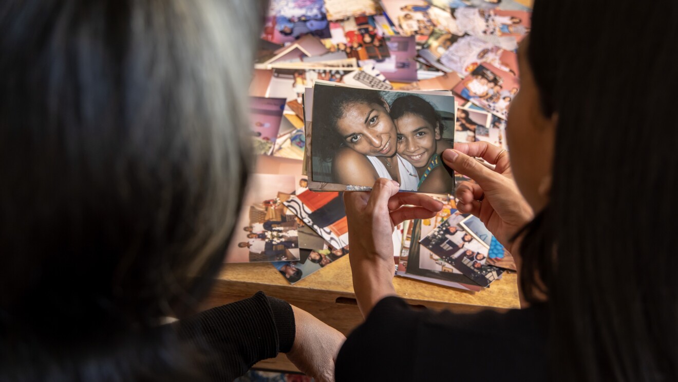 Two figures seen from behind look at a photo of a woman and a girl.