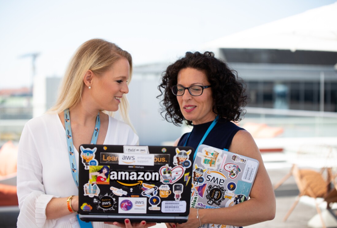 Zwei Frauen halten einen Laptop in den Händen auf dem Amazon steht. Sie sprechen miteinander.