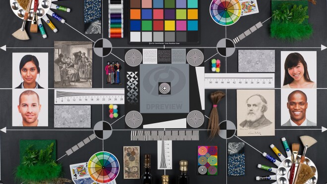 这个深灰色的矩形上有几十个物体和图像。所有这些产品都是用来测试新相机、镜头和智能手机的性能。有四张人物照片,两男两女,肤色各异。有各种各样的色块显示出彩虹的阴影。有旧的奥地利货币。有人造植物。还有各种详细的图案,包括西门子星。