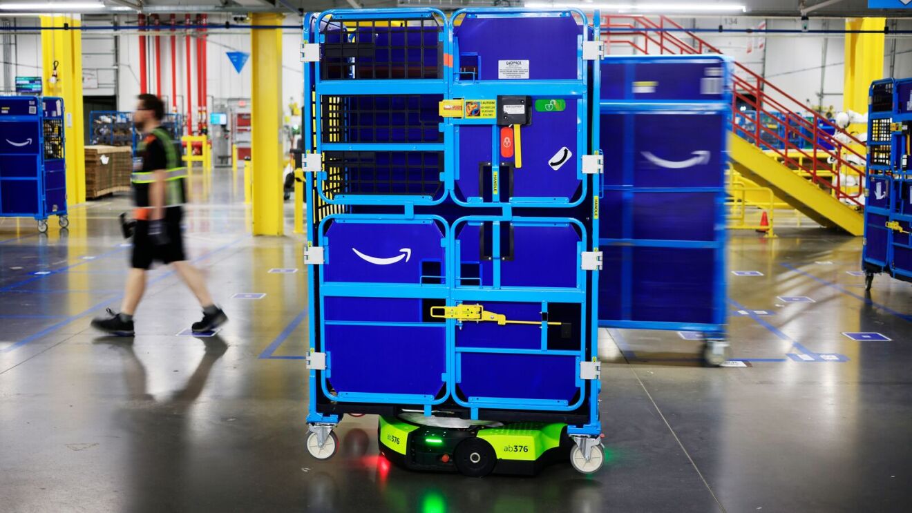 An employee at a fulfillment center alongside a robot transporting a cart