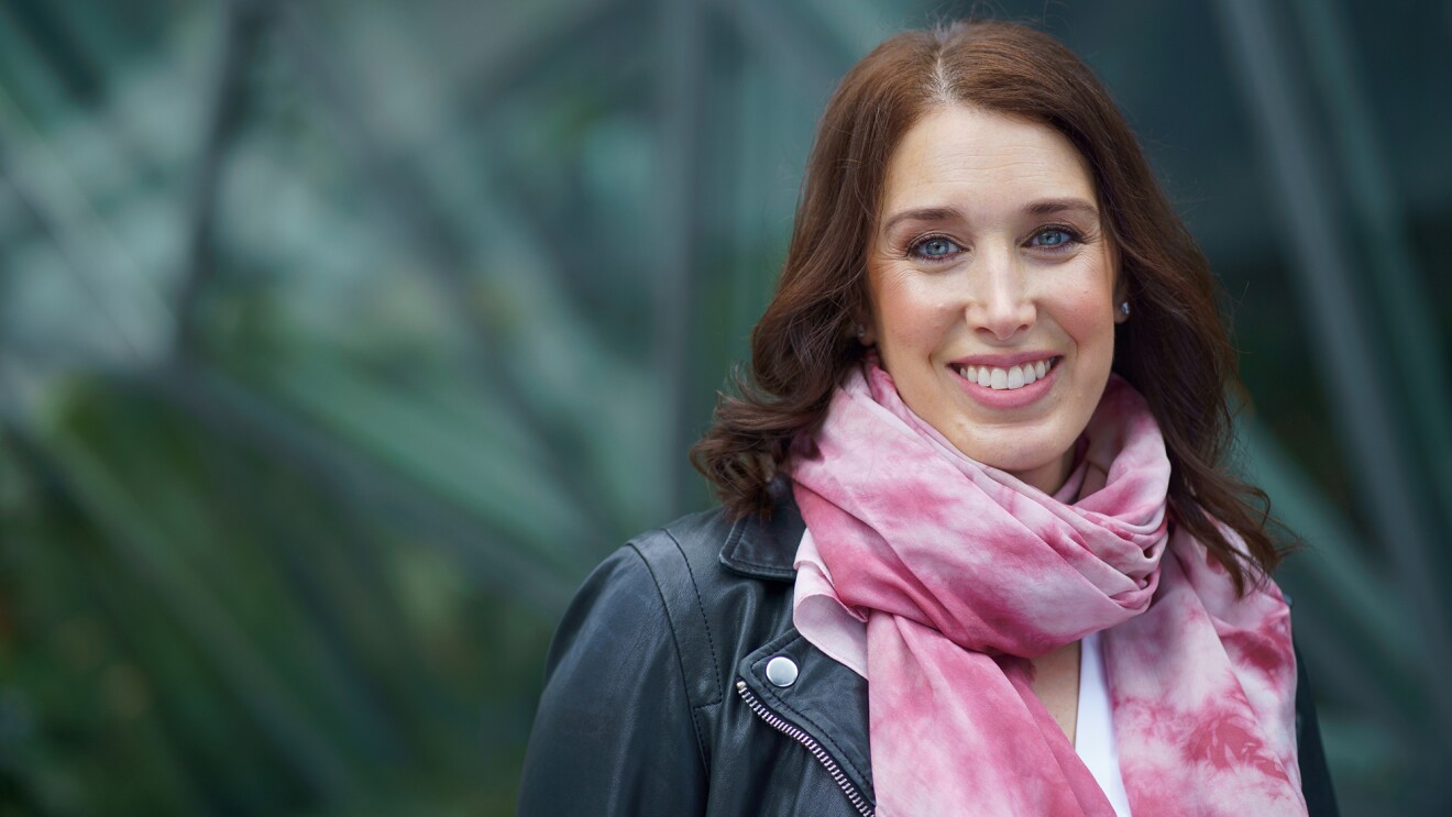 莎拉·格尔曼在西雅图亚马逊总部的“球体”前微笑着拍照。她戴着一条粉红色的围巾,穿着一件皮夹克。