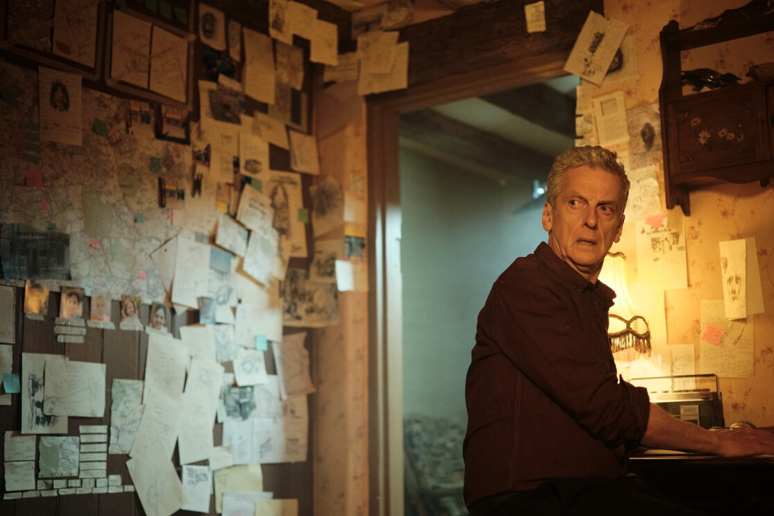 An elderly man with white hair stands in a room covered in papers