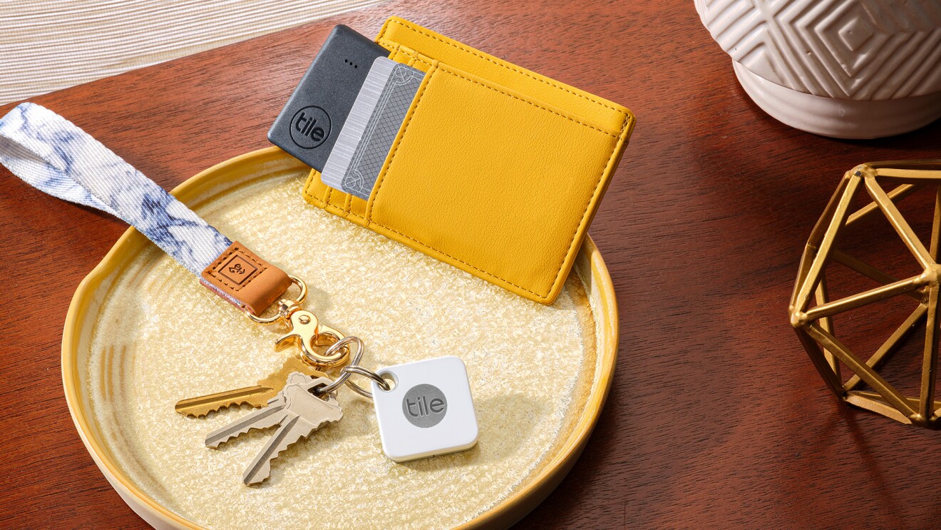 An image of a tray on a small table that holds keys with a hand-loop key ring and a Tile device. A wallet with credit cards in it sits next to the keys on the tray as well.