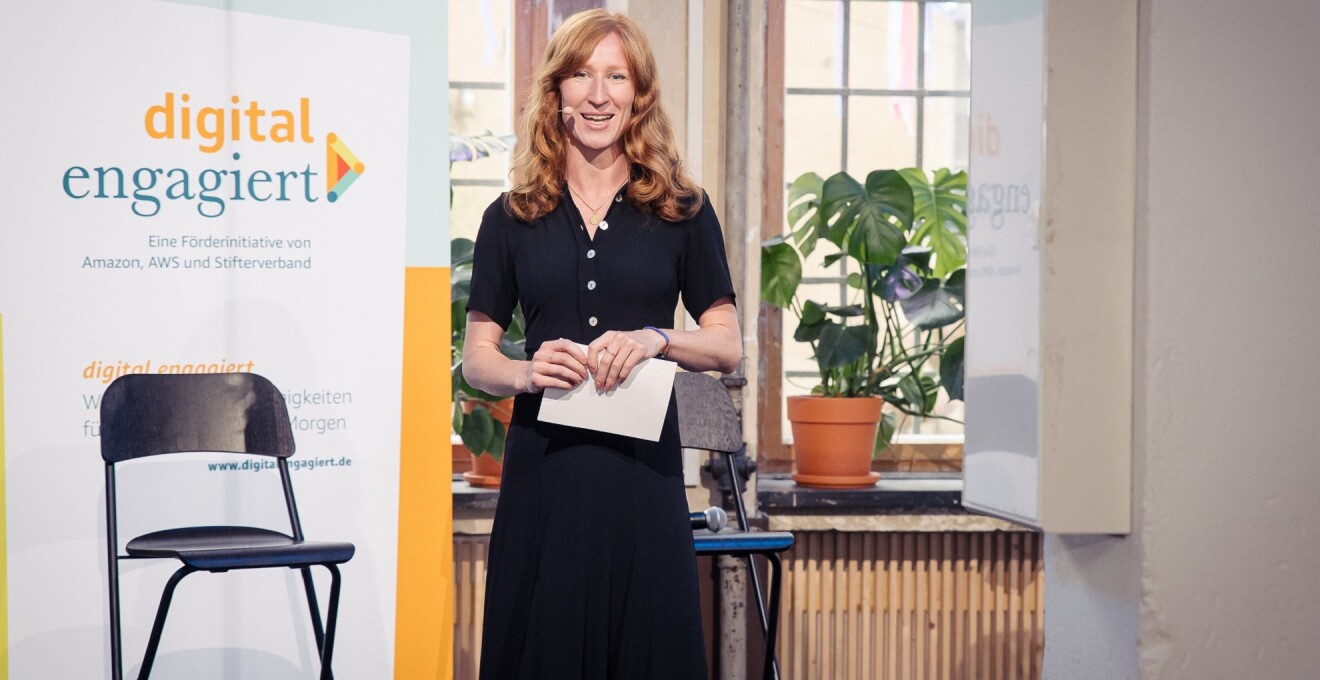 Die Moderatorin Teresa Sickert steht auf der Bühne der digital.engagiert-Abschluss-veranstaltung und spricht zum Publikum.