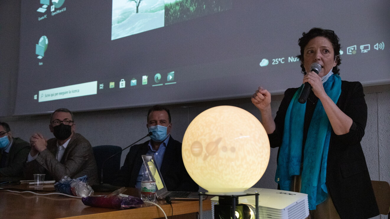 Foto di una donna di fronte ad un proiettore ed una riproduzione in miniatura della luna, illuminata. 