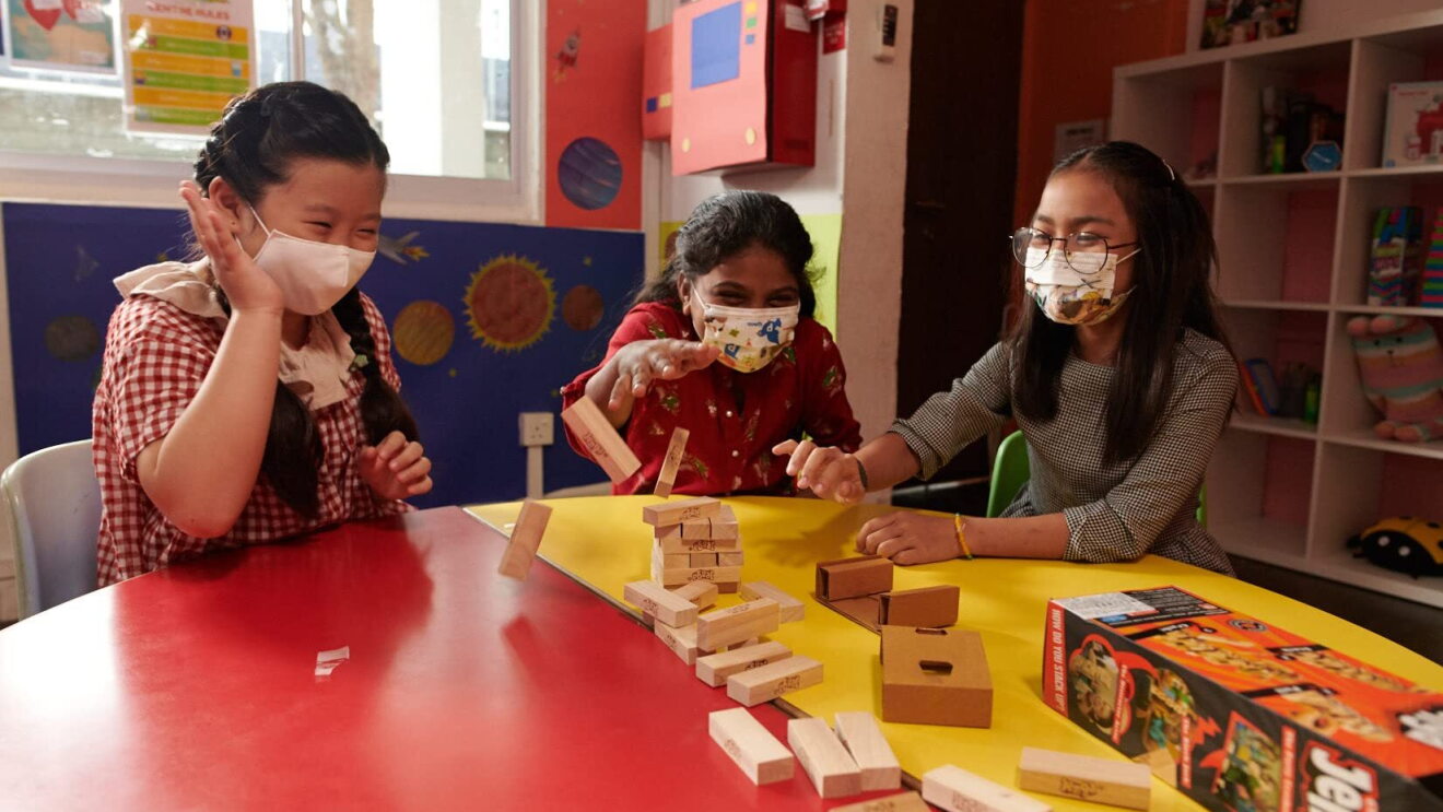 Children wear face masks and play with toys in a classroom-type setting