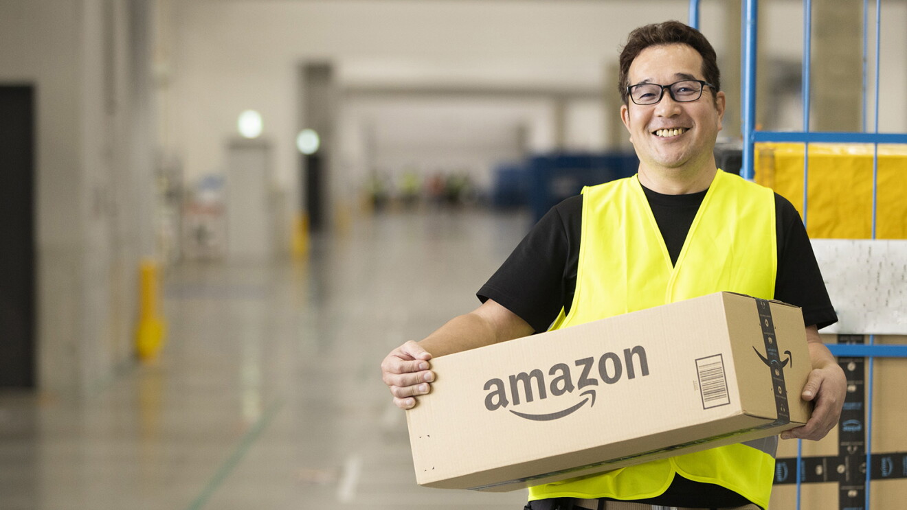 Amazonの段ボールを抱える男性（鈴木さん）黒いTシャツに黄色の作業用ベストを着ている