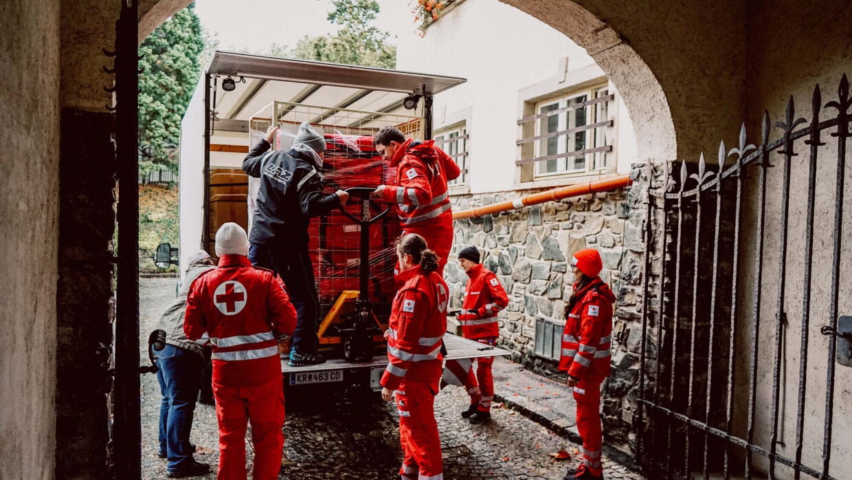 6 Mitarbeiter vom Roten Kreuz stehen hinter einem Rettungswagen. 