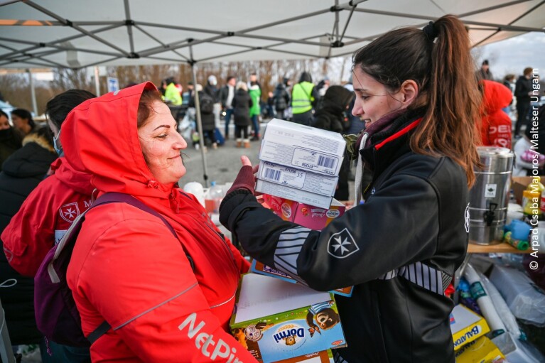 Eine Frau von Malteser überreicht einer Geflüchteten Nahrungsmittel.