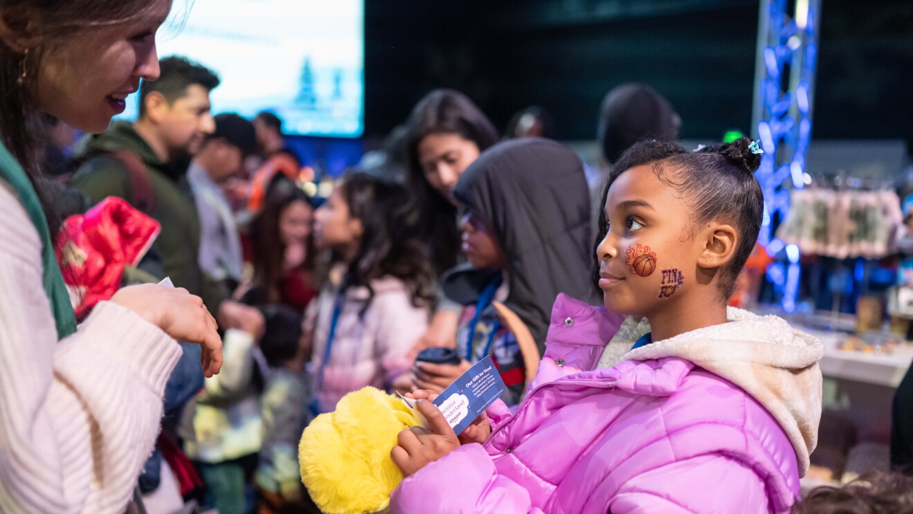Amazon’s Winter Wonderland: Child holding yellow plush toy among diverse crowd