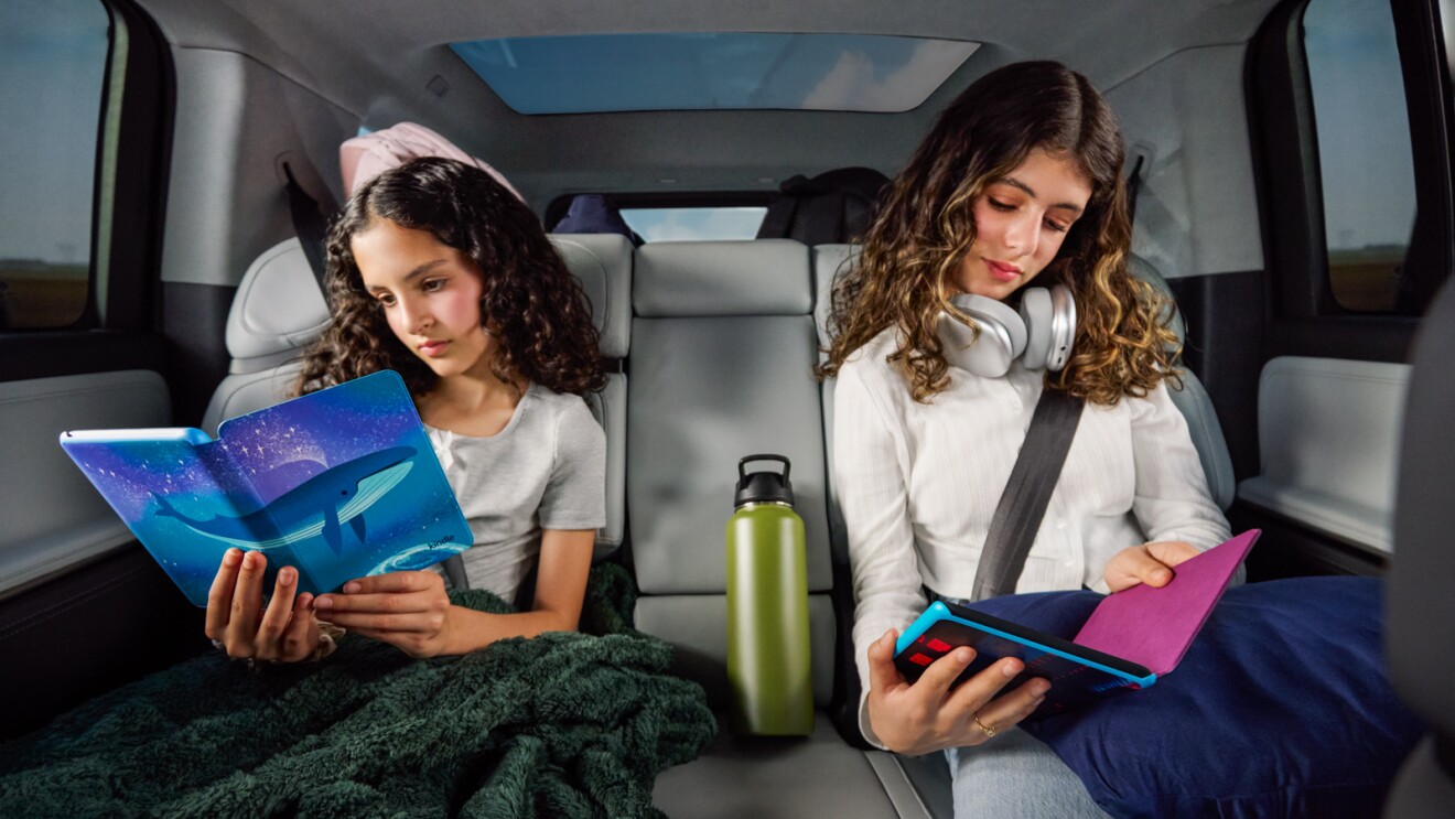 Siblings engrossed in reading during car journey, green water bottle between them