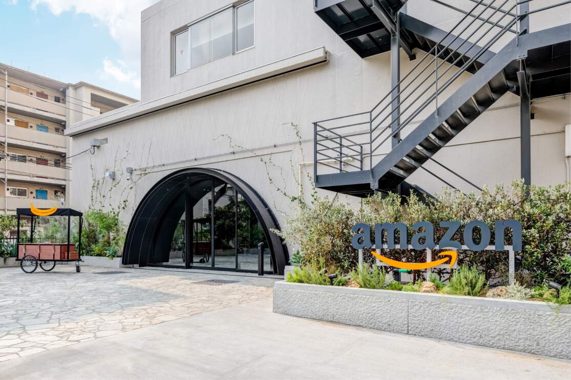 白い建物に黒い半円形の入口がついている。その横にAmazonのロゴマークと非常階段
