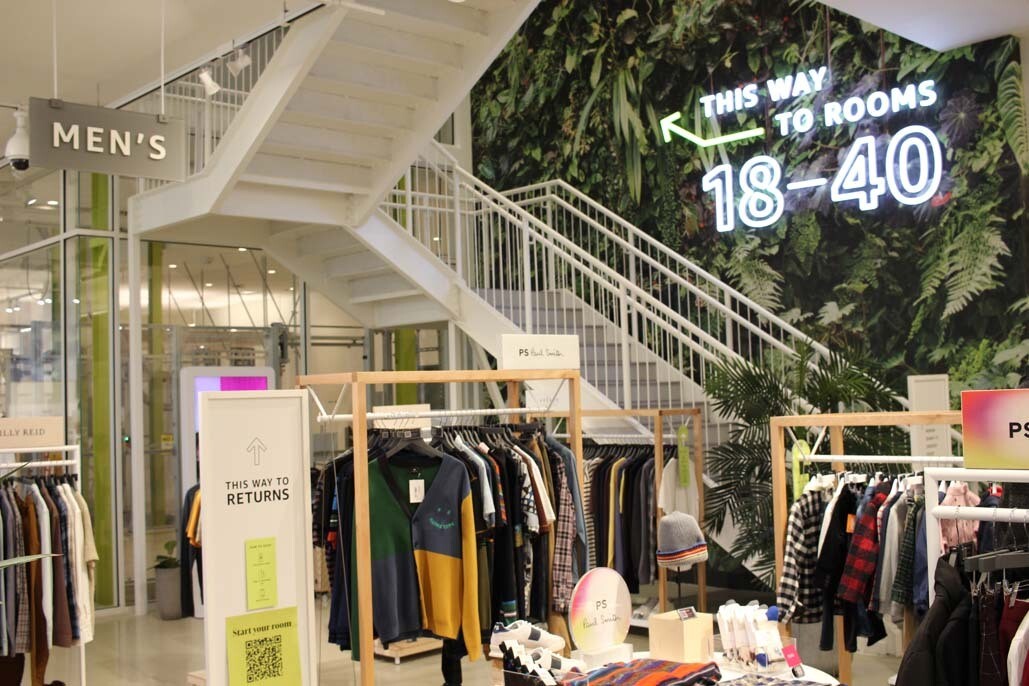 An image of clothing racks and stairs leading to a second floor of the Amazon Style store.