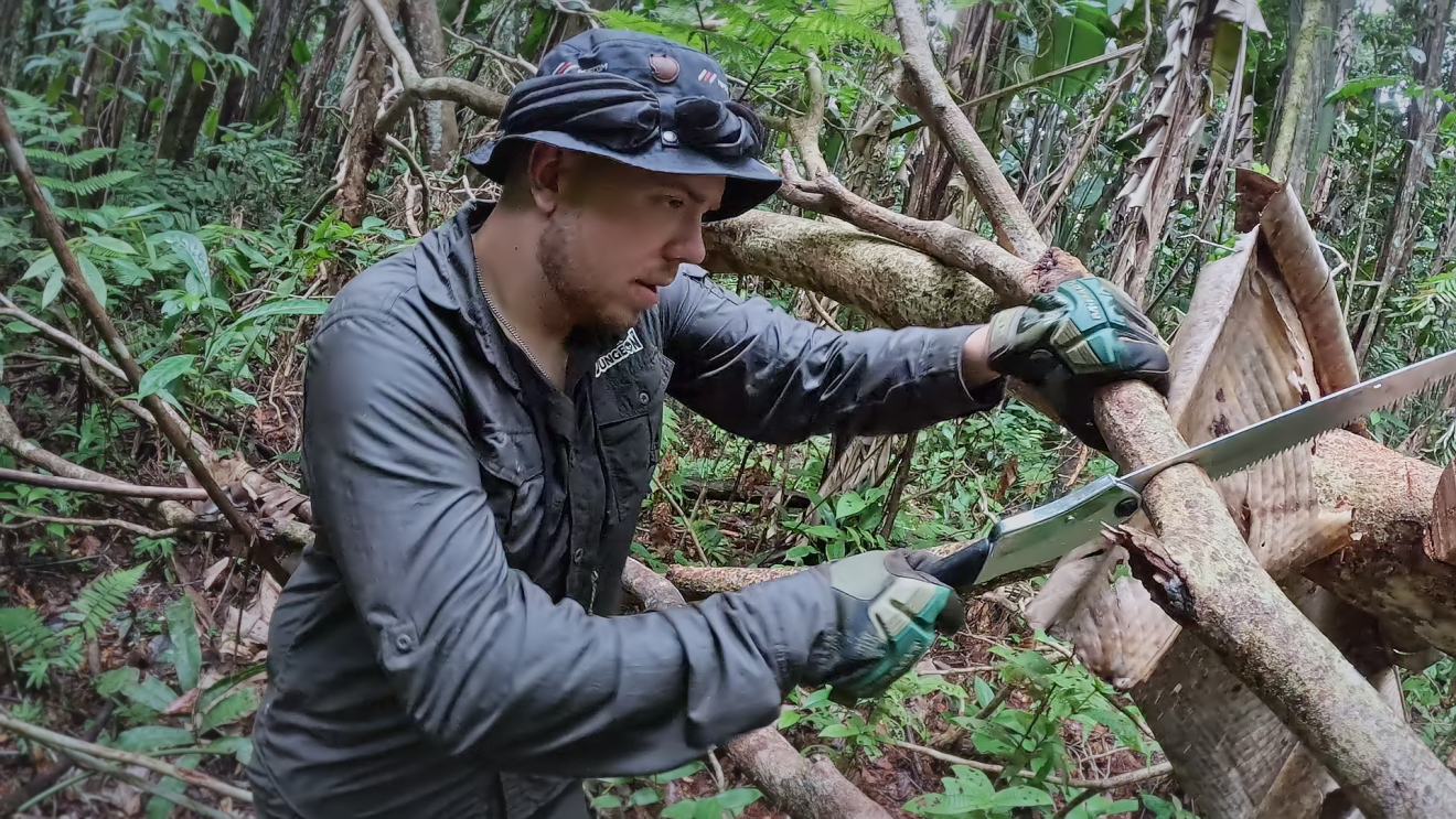 7 vs. Wild Teilnehmer sägt an einem Baum im Dschungel