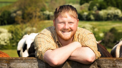 Cheerful farmer in plaid shirt resting arms on pasture fence