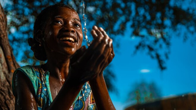 图像的一个年轻女孩微笑,握着她的手感觉源源不断地从喷口水。